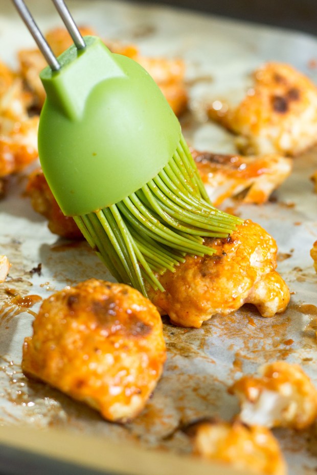 Basting roasted cauliflower pieces with buffalo wing sauce